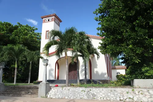 A white stucco chapel with red tile roof stands amidst palm trees