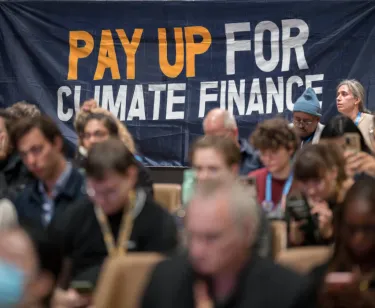 People sitting in front of a Pay Up For Climate Finance Sign