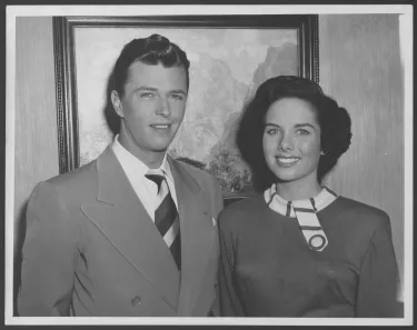 Colleen stands on the right next to a man dressed in a suit jacket and a tie.