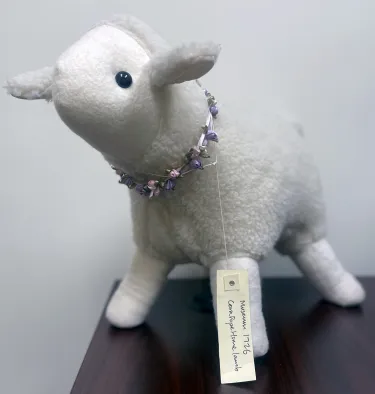 Stuffed lamb with a faux flower wreath around her neck and a tag that reads Museum Collection, Cora J Pope Home.