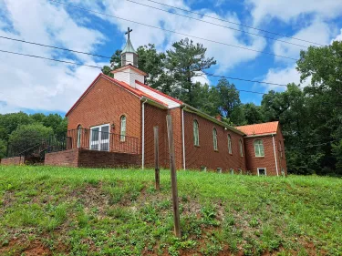 Photograph shows a red brick church building, a blue sky filled with clouds behind it.