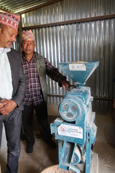 Men standing at a grain mill with Presbyterian Disaster Assistance labeled on it