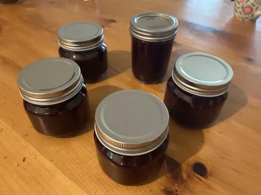 Five jars of blackberry jam on a kitchen table
