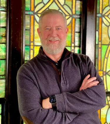 Portrait of man standing with hands folded in front of stained glass