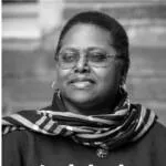 Black and white headshot of Arelis Figueroa wearing a plaid scarf and wire-framed glasses