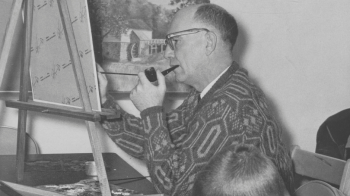 A man smoking a pipe paints a canvas on a desktop easel, while at his side a young boy leans his head on his arm and draws.