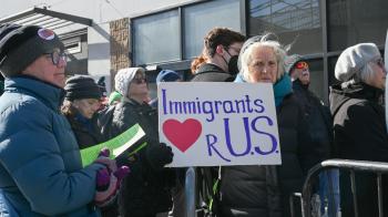 Vigil participant stands with sign outside of Philadelphia Immigration and Customs Enforcement Offices. 