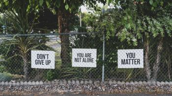 Signs with uplifting statements near a fence and lush vegetation 
