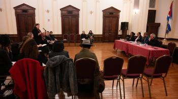 A large room with people sitting in a circle of chairs facing four people sitting at a table.