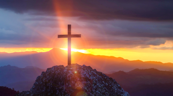 Cross on top of mountain with sunlight beaming behind it