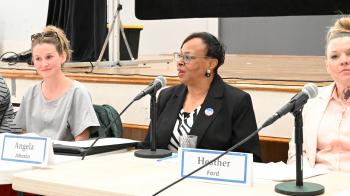 A woman wearing a dark blazer and black and white shirt speaks while flanked by others at a panel discussion.