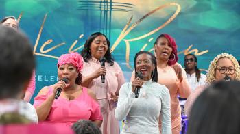 A colorfully dressed choir sings in front of a He Is Risen backdrop of turquoise and gold.