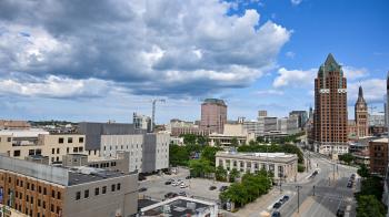 A view of Downtown Milwaukee from four stories up with several tall buildings forming the skyline and billowing clouds above.