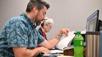 person in paisley shirt with ear buds looking at papers while talking