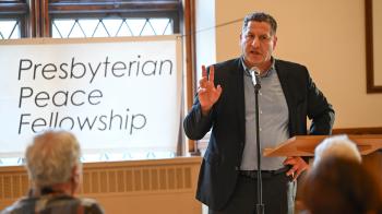 speaker in front of Presbyterian Peace Fellowship sign