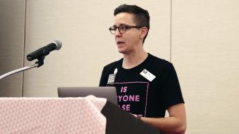 A person in a black t-shirt stands at a microphone