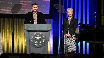A man stands on stage at a podium and a woman stands to his left