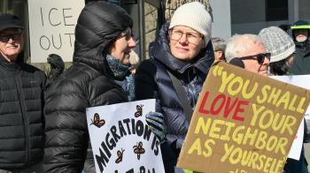 Protestors stand outside in coats and hats holding signings advocating for immigrants 