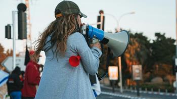 woman in a jacket and hats speaks into a megaphone