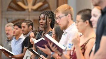 A group of young adults stand and sing in a chapel 