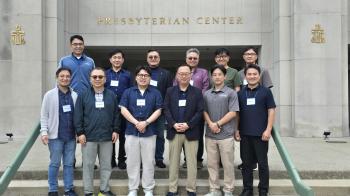 A group of Korean American people stand on the steps of a building with a sign that says "Presbyterian Center" behind them.
