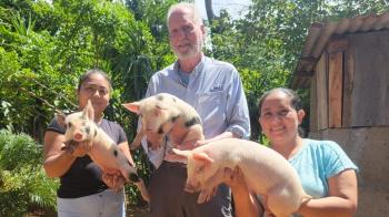 A man and two women holding pigs while standing outdoors
