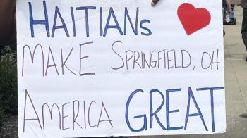 A handmade sign held by a Black man says "Haitians make Springfield, OH and American Great"