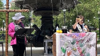 Tamar Wasoian holds a broken piece of bread above a communion table in the Boston Common. To her right, another pastor preachers from a stand.