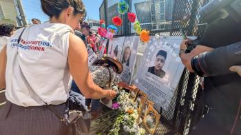 People gather around a memorial with flowers and crosses.