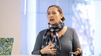 A woman in front of windows speaks to a crowd