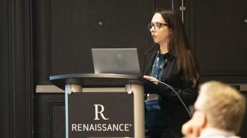 A young woman speaks at a hotel lectern with her laptop computer open