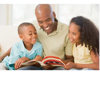 A father with his son and daughter looking at a book together. 