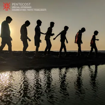A group of children silhouetted walking in a line down by a lake. 