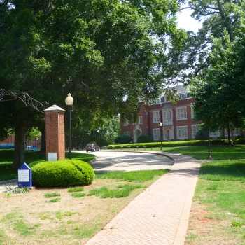 A pathway leads to a brick building obscured by trees