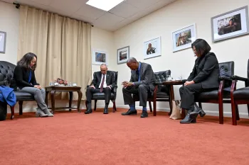 Four people in a large room with their heads bowed in prayer.