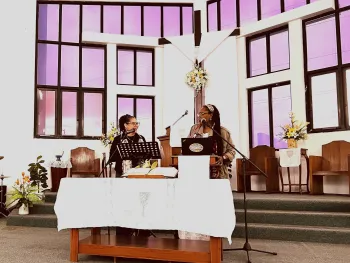 Two women standing at communion table facing each other smiling