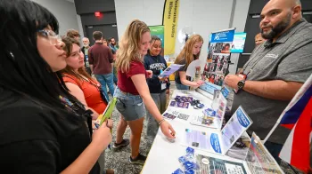 A group of people gather around a table with pamphlets and swag