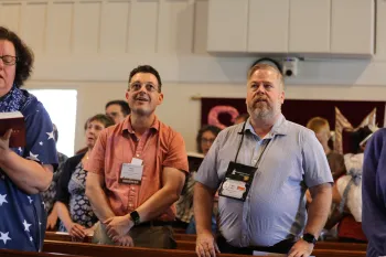 two people standing facing the front of sanctuary during worship