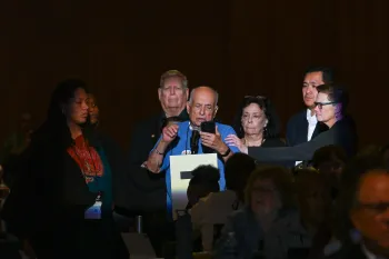 person reading from phone into microphone flanked by people to sides and back