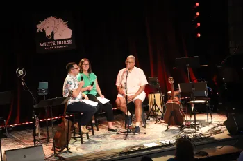 Three people talk on a stage during a live recording of a podcast