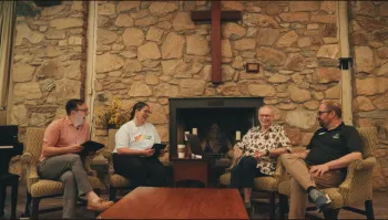 A group of four people have a conversation in front of a stone wall