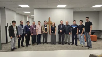 A group of Korean American people stand in a line in front of an artistic representation of a cross.