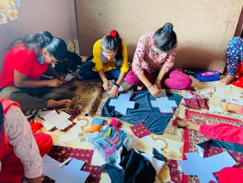 This image shows Nepali women sitting on the floor in a circle sewing sanitary pads