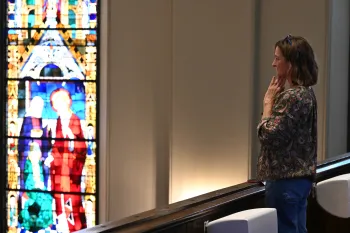 A woman stands in a church balcony next to a stained glass window