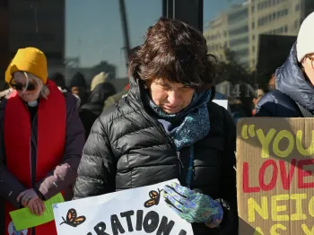 Vigil prays while holding a sign in support of immigrants. 