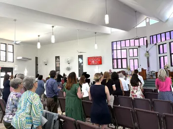 The backs of a group of people standing during worship in a bright chapel