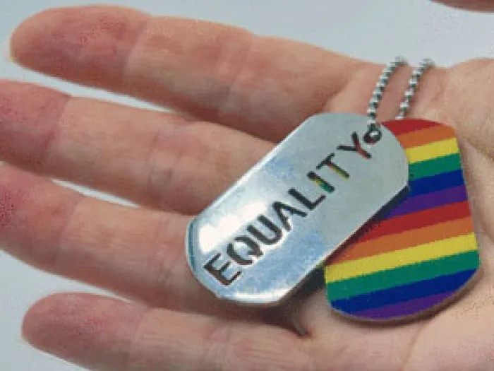 Hand holding a dog tag with equality written on it and rainbow heart