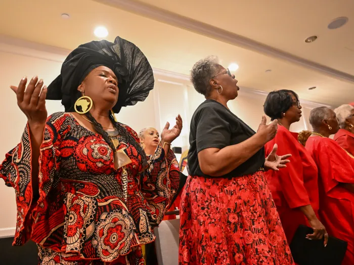 A portion of a choir, including woman in large hat, sings