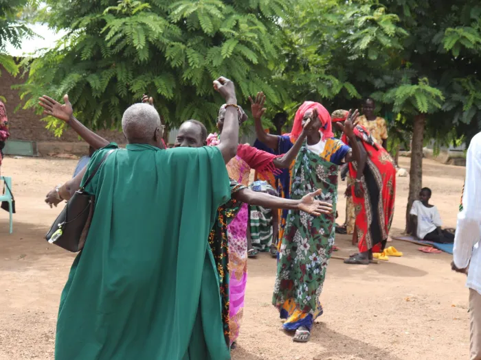 Woman in flowing green garments greets other women in bright prints