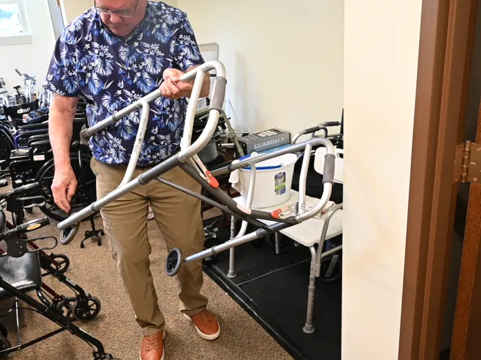 A man carries a walker out a room full of walkers and other mobility equipment.